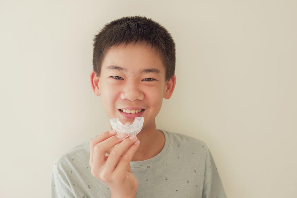 A young boy is holding a dental model with clear aligners