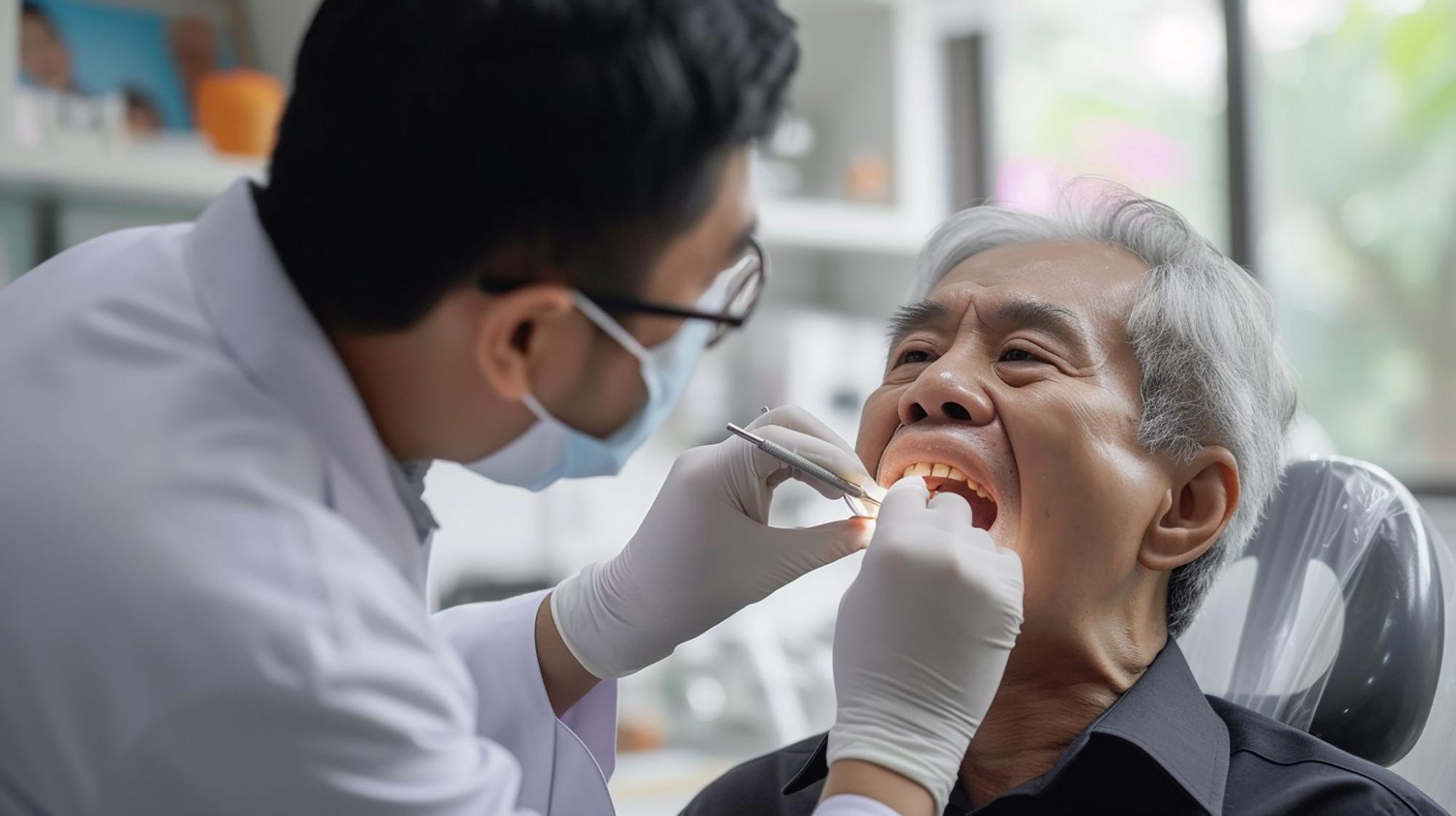 an Asian male dentist performs an oral examination on an elderly man’s teeth